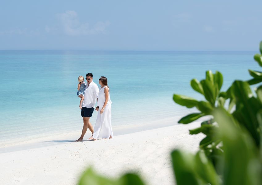 A family holding hands and walking along the white sand beach in the Maldives